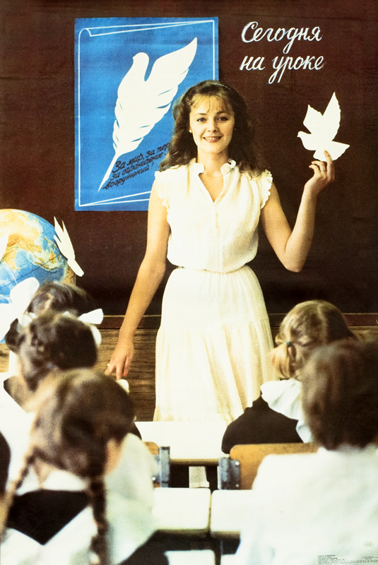 Photo of teacher in front of classroom holding a dove cutout; brown, white, blue