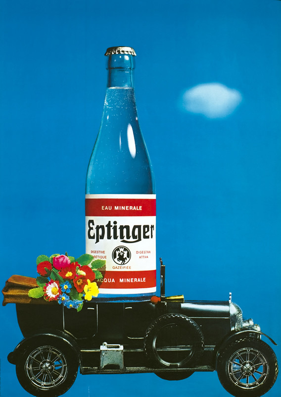 Black toy car, convertible, with flowers and an Eptinger bottle in front seat; blue background, red, black, yellow & white