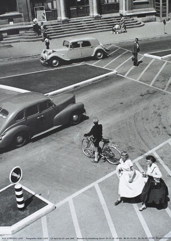 Circa 1950s street scene of cars and pedestrians; black, white, gray