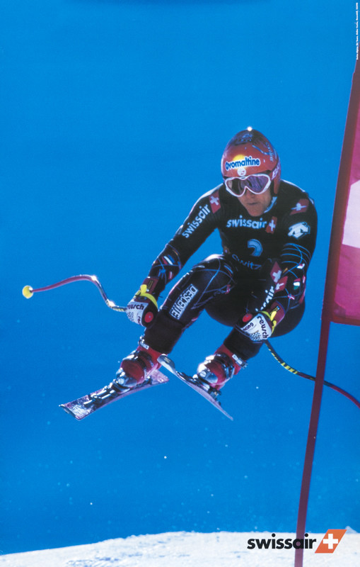 Airborne racing skiier dodges flag; blue, white, red, black